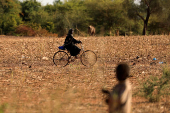 FILE PHOTO: A child who fled with his parents from attacks of armed militants in the Sahel region watches a woman on a bicycle at a camp for internally displaced people (IDPs) in Kaya