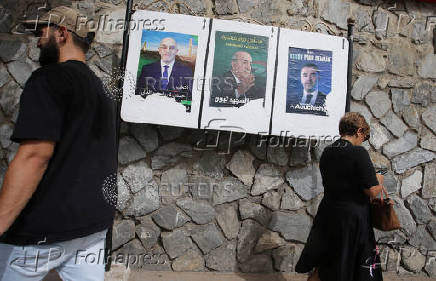 People walk past electoral campaign posters of presidential candidates in Algiers