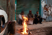 Labourers keep themselves warm near a fire on a cold winter morning, along a market in Karachi