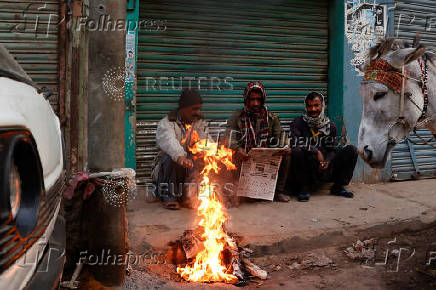 Labourers keep themselves warm near a fire on a cold winter morning, along a market in Karachi