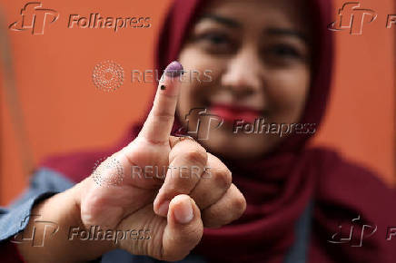 A woman shows an ink-stained finger after casting her vote at a polling station during regional elections in Jakarta