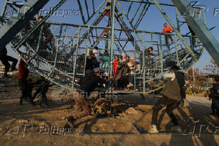 A man pushes the swing boat as children sit inside, at an amusement park, in Douma