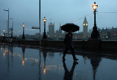 People shield from rain during morning rush-hour near Houses of Parliament, in London