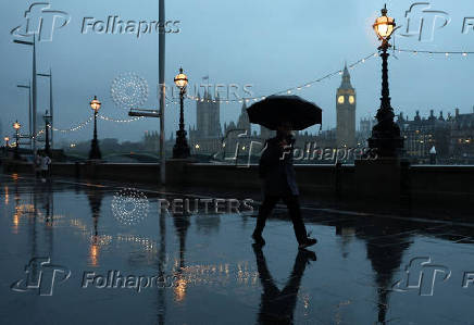 People shield from rain during morning rush-hour near Houses of Parliament, in London