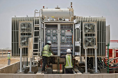 Workers install an electric transformer at the Khavda Renewable Energy Park of Adani Green Energy Ltd (AGEL), in Khavda
