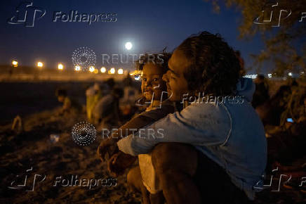 A migrant man caresses his son along the bank of the Rio Grande river in Ciudad Juarez