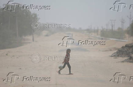 A girl crosses a road amidst dust on a hot summer day in Barmer