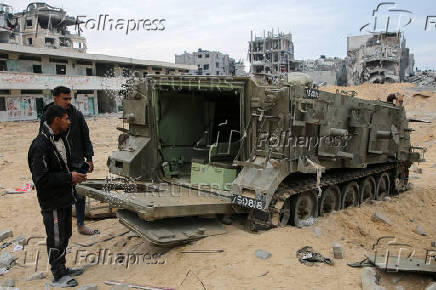 Palestinians look at damaged Israeli military vehicles left behind by Israeli forces in Rafah