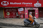 FILE PHOTO: A woman rides her scooter past a Muthoot Finance branch in Ahmedabad