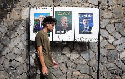 A person walks past electoral campaign posters of presidential candidates in Algiers