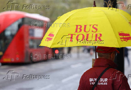 A bus tour vendor holds an umbrella in London