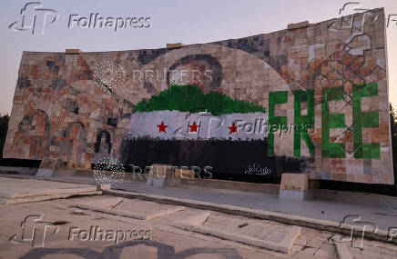 People stand  beside graffiti of the Syrian rebels flag painted on a mosaic of former Syrian president Hafez al-Assad  in Damascus