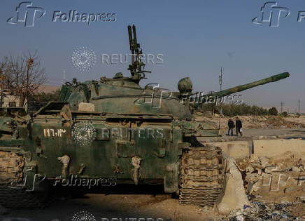 Men walk near an abandoned tank that belongs to the ousted Syrian President Bashar al-Assad's forces, on the outskirts of Damascus