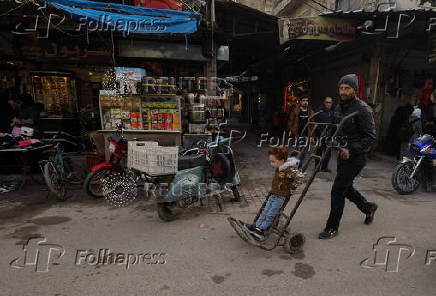 A man pushes a boy standing on a cart along the market , in Douma