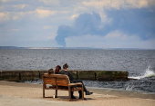 People rest on beach as smoke rises over port of Pivdennyi after Russian strike seen from Odesa