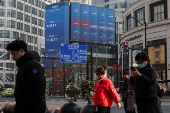 Pedestrians wait for a street signal on a sidewalk as an electronic billboard shows the Shanghai and Shenzhen stock indexes in Shanghai