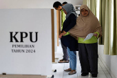 A blind woman with her helper votes at a polling station during regional elections in Jakarta