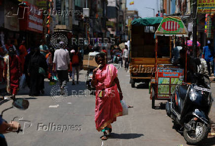 A woman takes a bite of an ice cream as she walks along the market during a hot day in Bengaluru
