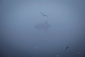 People ride a boat across the Yamuna river on a foggy winter morning in New Delhi