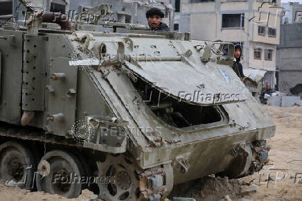 Palestinians look at damaged Israeli military vehicles left behind by Israeli forces in Rafah