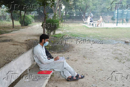 A man uses a face mask to avoid smog, while reading book at a park in Lahore