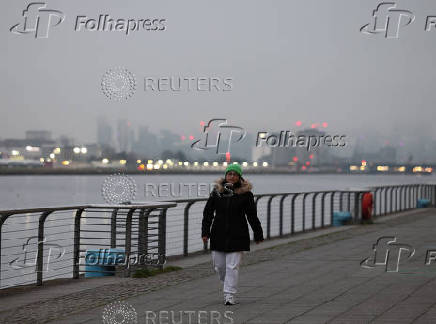 A woman walks by the Royal Docks during foggy weather in London