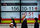 Passersby walk in front of an electric screen displaying the current Japanese Yen exchange rate against the U.S. dollar in Tokyo