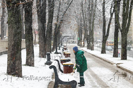 Municipal worker removes snow from benches in a park during a snowfall in Kyiv