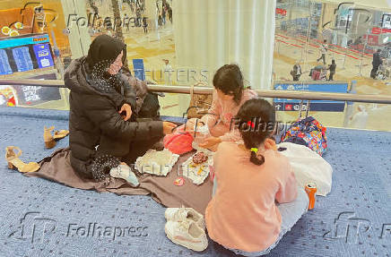 A woman with her daughters eats as they wait for their flight after a rainstorm hits Dubai, causing delays at the Dubai International Airport