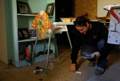 Woman holds pictures, as she crouches, inside of a building, in a damaged neighbourhood near the Israel-Lebanon border in Manara