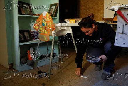 Woman holds pictures, as she crouches, inside of a building, in a damaged neighbourhood near the Israel-Lebanon border in Manara