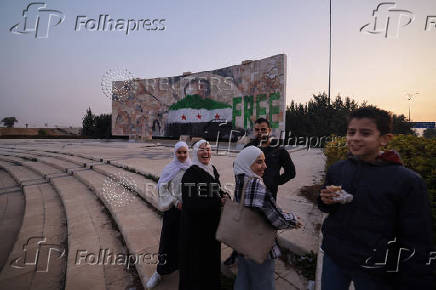 People stand near a graffiti of the Syrian rebels flag painted on a mosaic of former Syrian president Hafez al-Assad  in Damascus