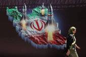 An Iranian woman walks past an anti-Israel banner with a picture of Iranian missiles on a street in Tehran