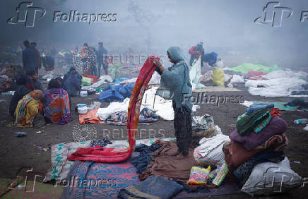 A girl folds her blanket as others sit next to a fire at an open ground on a foggy winter morning in the old quarters of Delh