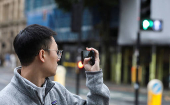 A man takes a photo of the road, using his smartphone in Manchester