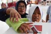 A blind woman with her helper votes at a polling station during regional elections in Jakarta