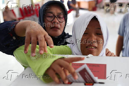 A blind woman with her helper votes at a polling station during regional elections in Jakarta