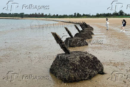 A woman poses for pictures next to anti-landing barricades on a beach in Kinmen Island