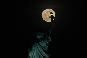 A Lua Rosa (primeira lua cheia da primavera) iluminada em 100 por cento surge atrs da Esttua da Liberdade na cidade de Nova York