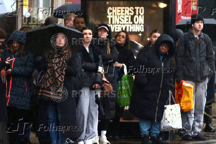 People wait at a bus stop during a rain shower in London