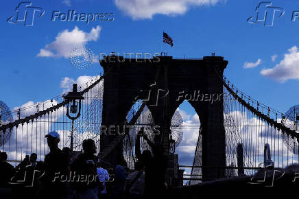 People pose for photographs as other walk on the Brooklyn Bridge in New York City