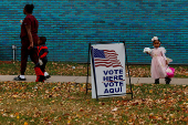 People participating in Halloween festivities walk past a voting sign outside the River Rouge Civic Center in the Wayne County suburb of Detroit, Michigan