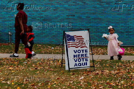 People participating in Halloween festivities walk past a voting sign outside the River Rouge Civic Center in the Wayne County suburb of Detroit, Michigan