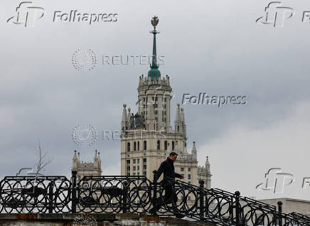 A man walks along at the bridge, with a Soviet era skyscraper seen in the background, on a rainy day in Moscow
