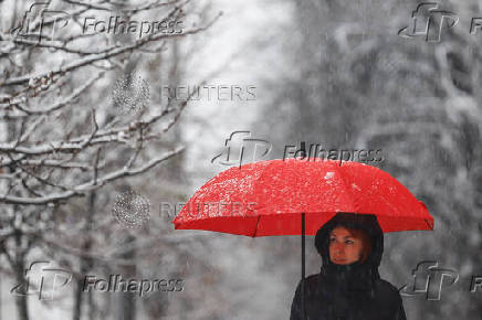 Woman with an umbrella walks along a street during a snowfall in Kyiv