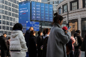 Pedestrians wait for a street signal on a sidewalk as an electronic billboard shows China's 2024 GDP growth in Shanghai