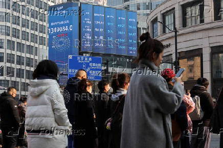 Pedestrians wait for a street signal on a sidewalk as an electronic billboard shows China's 2024 GDP growth in Shanghai