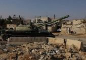 People sit near an abandoned tank that belongs  to the ousted Syrian President Bashar al-Assad's forces, on the outskirts of Damascus