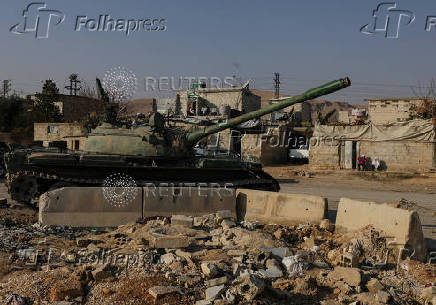 People sit near an abandoned tank that belongs  to the ousted Syrian President Bashar al-Assad's forces, on the outskirts of Damascus