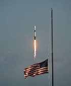 An American flag flies at half staff in honor of former President Jimmy Carter at the Kennedy Space Center press site as a SpaceX Falcon 9 rocket lifts off from the Cape Canaveral Space Force Station